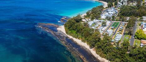 Ein Luftbild von Jervis Bay mit einer Küstenstraße, Strand und Campingplätzen.