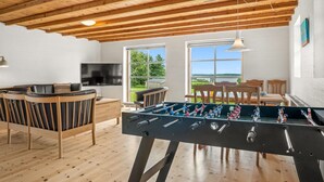 Una stanza con un tavolo da calcio, pavimento in legno, televisione e ampie finestre con vista.