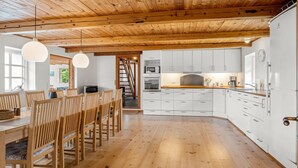 Una cucina moderna con mobili bianchi, pavimento in legno e soffitto in legno.