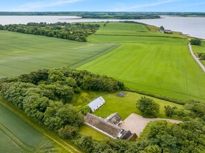 An aerial view of a rural property with expansive green fields, a small building with a thatched roof, and a body of water in the background. - "Åsta" - 400m to the fjord by Interhome (Roslev)