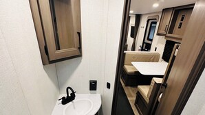 A compact bathroom with a sink, toilet, and a mirror above the sink. - Cozy RV in Welcoming San Diego with WiFi, AC (San Diego)