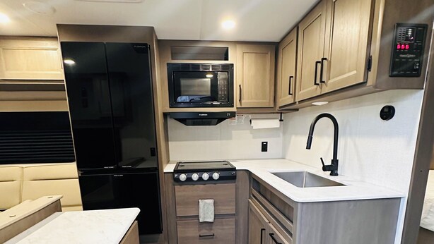 A compact kitchen with a microwave, stove, sink, and wooden cabinets. - Cozy RV in Welcoming San Diego with WiFi, AC (San Diego)