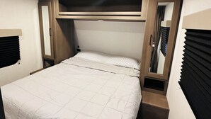 A neatly made bed with a headboard, a small bedside table, and a mirror. - Cozy RV in Welcoming San Diego with WiFi, AC (San Diego)