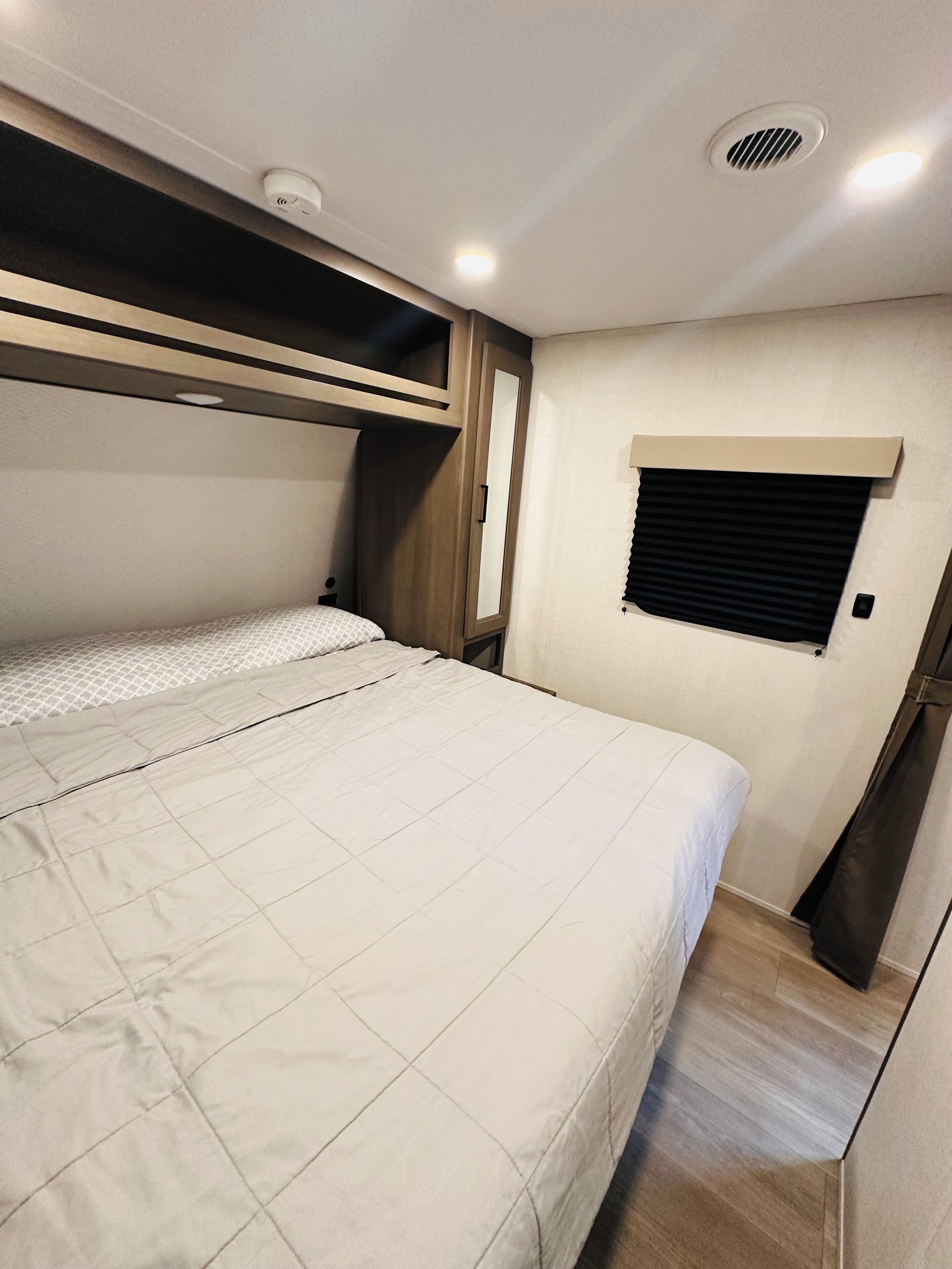 Un dormitorio con cama, ventana con persianas, rejilla en el techo y cabecera de madera.