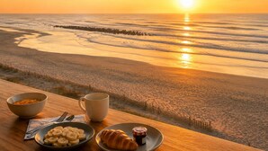 Ein Tisch mit Frühstücksangeboten und Blick auf den Sonnenuntergang über dem Meer.