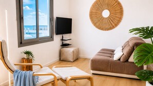 Ein modernes Wohnzimmer mit einer Couch, einem Fernseher, einer Wanddekoration, einer Pflanze und Meerblick durch ein Fenster.