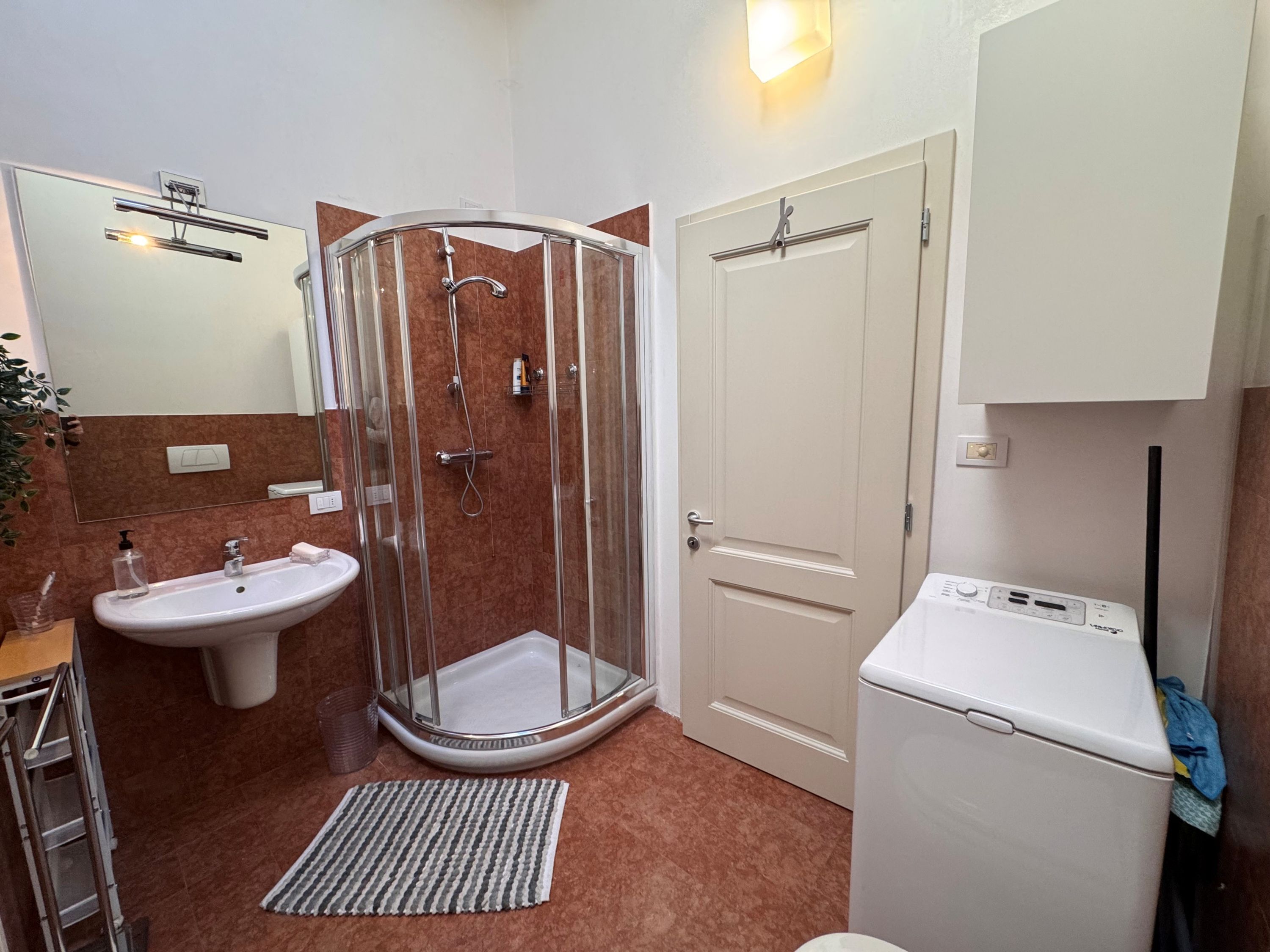 Un bagno con doccia vetro, lavandino, water e lavatrice.