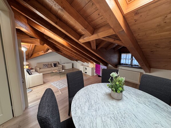 Un loft espacioso con techo alto y vigas de madera a la vista. Cuenta con una mesa redonda de mármol con una planta en maceta, un sofá y una mesita de centro.