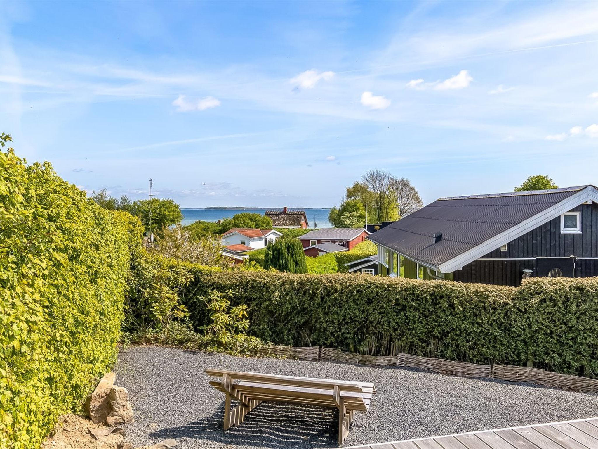 A wooden bench in a gravel area with a view of a coastal town and a body of water.