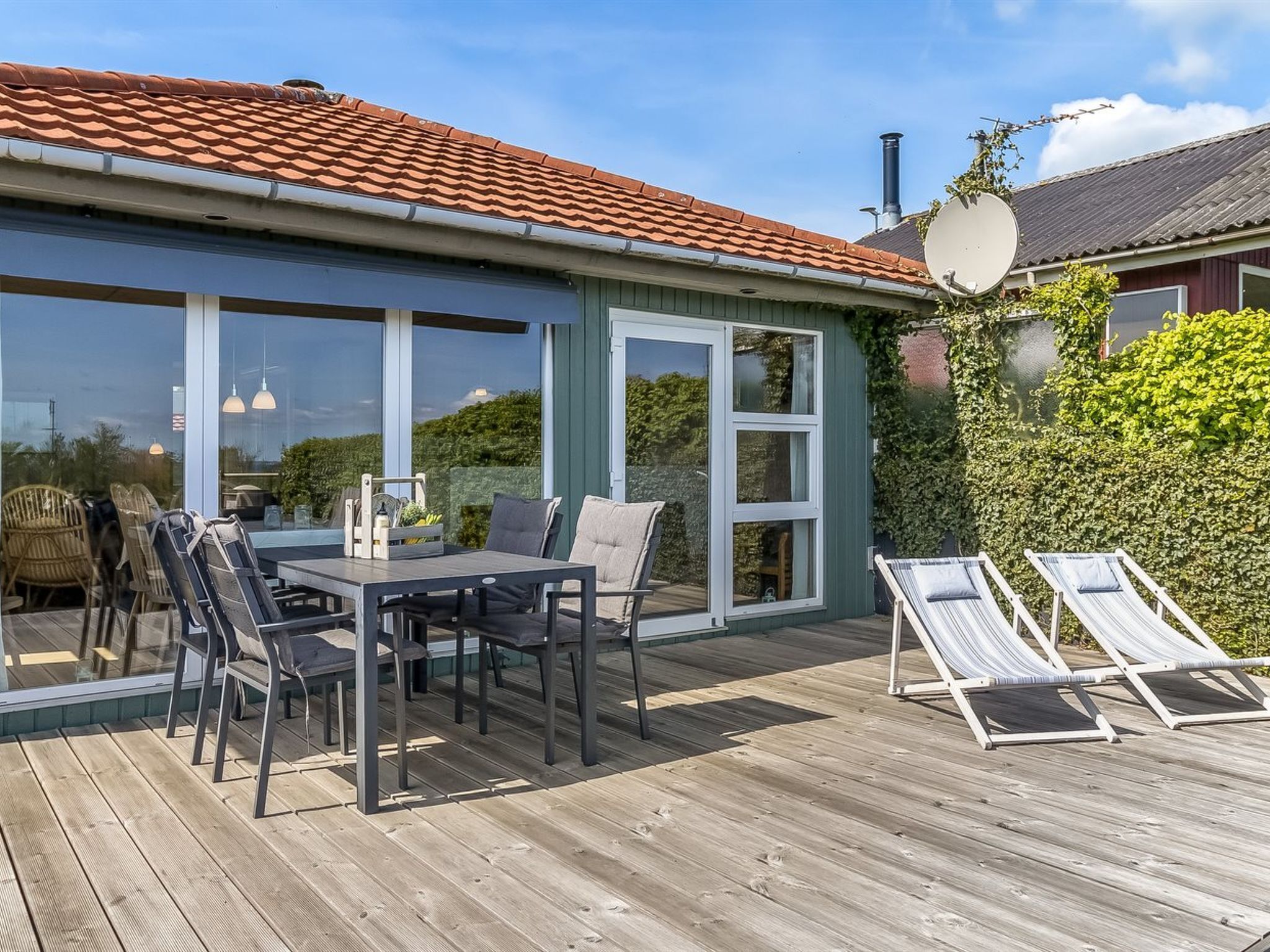 Eine Holzterrasse mit Tisch, Stühlen und zwei Liegestühlen sowie einer Glastür.