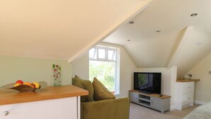 Ein gemütliches Schlafzimmer im Loft-Stil mit Bett, Fernseher, Sofa und Essecke mit Obstschale.