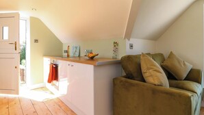 Ein gemütlicher Wohnbereich mit Holzboden, einem grünen Sofa und einer Küchenzeile mit Holzarbeitsplatte.