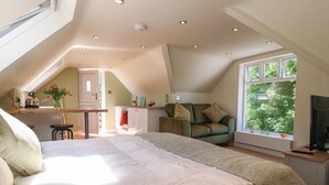 Ein Schlafzimmer mit einem großen Bett, einem Schreibtisch, einem Stuhl und einem Fenster mit Blick auf Bäume.