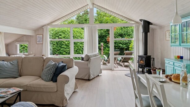 A cozy room with a high ceiling, a sofa, a dining table, and a view of the garden through large windows. - "Tekla" -  from the sea by Interhome (Rørvig)