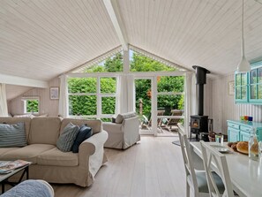 A cozy room with a high ceiling, a sofa, a dining table, and a view of the garden through large windows. - "Tekla" -  from the sea by Interhome (Rørvig)