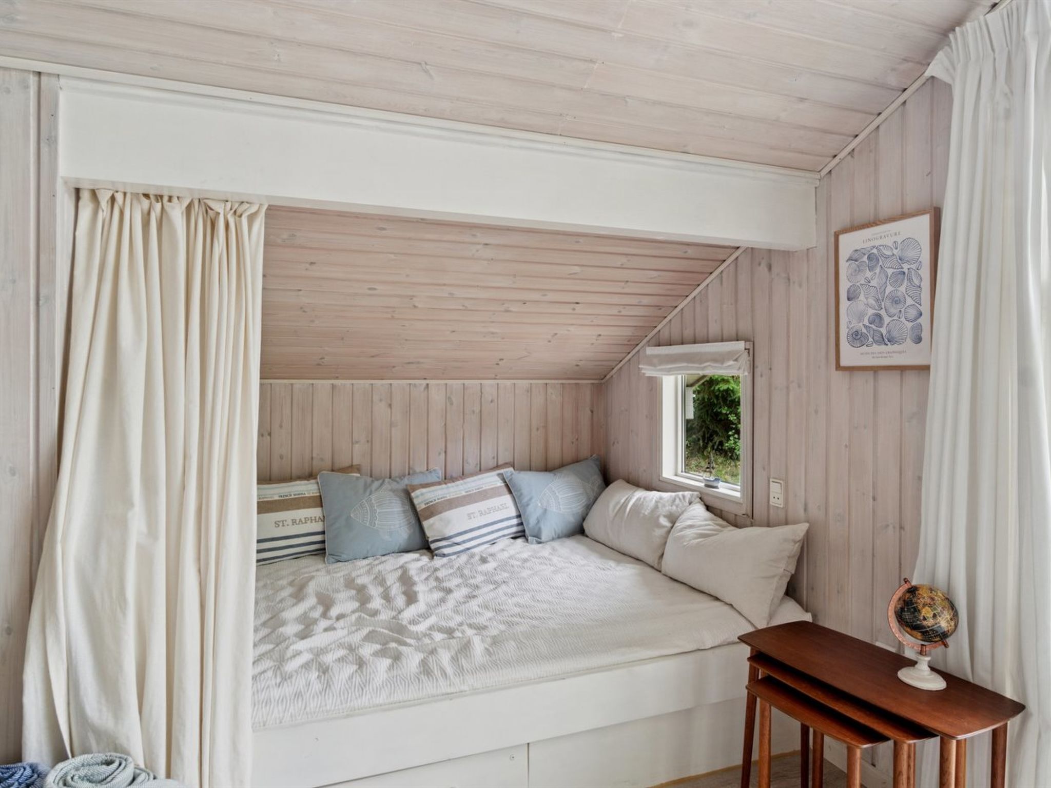 Une chambre confortable avec un plafond en pente, un lit avec une literie à rayures, une petite table sur laquelle repose un globe terrestre et, au mur, une illustration botanique encadrée.