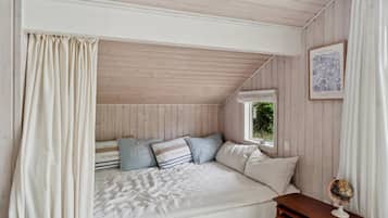 Une chambre confortable avec un plafond en pente, un lit avec une literie à rayures, une petite table sur laquelle repose un globe terrestre et, au mur, une illustration botanique encadrée.