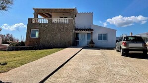 A two-story house with a stone facade and a balcony, a car parked in the driveway, and a clear blue sky. - Villa Miramar. Spectacular views. (Es Mercadal)