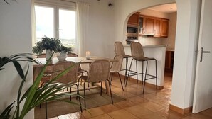 A dining area with wicker chairs and a table, a kitchen with wooden cabinets and a microwave, and a view through an archway. - Villa Miramar. Spectacular views. (Es Mercadal)