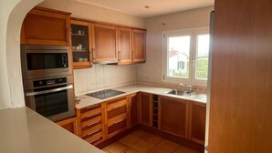 A kitchen with wooden cabinets, a built-in oven, a microwave, and a sink. - Villa Miramar. Spectacular views. (Es Mercadal)
