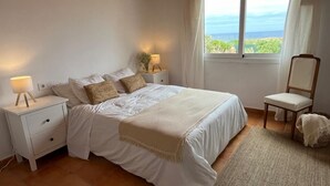 A bedroom with a bed, nightstands, a chair, and a view of the ocean. - Villa Miramar. Spectacular views. (Es Mercadal)