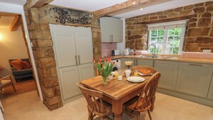 Une cuisine chaleureuse avec un mur en pierre, une table à manger en bois et des chaises. Une fenêtre offre une vue sur la verdure environnante.