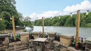 Une terrasse extérieure avec des murs en pierre, des chaises en métal, une table et des guirlandes lumineuses.