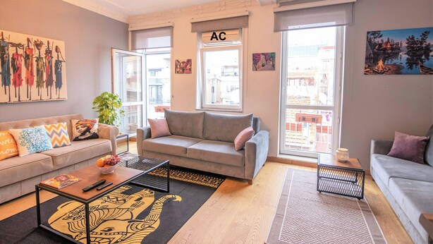 Uma sala de estar moderna com um sofá cinza, uma mesa de centro e uma janela grande com um aviso de 'ar condicionado'.