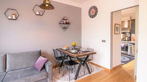 Uma sala de estar moderna com um sofá cinzento, uma mesa de jantar de madeira com cadeiras e prateleiras hexagonais decorativas na parede.