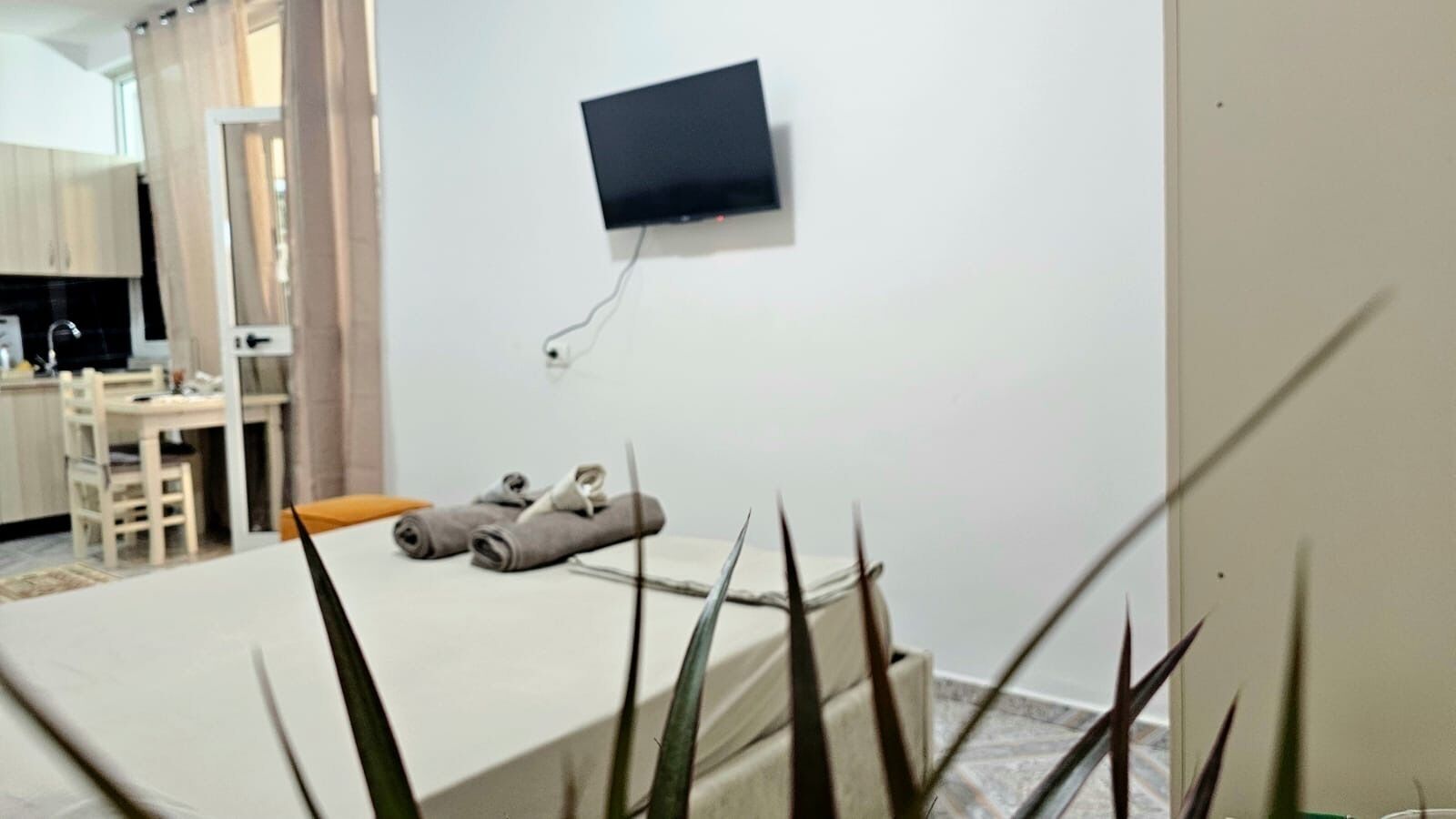 A bedroom with a bed, a TV mounted on the wall, and a small table with towels.
