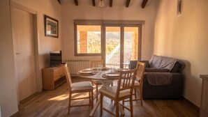 Un coin repas avec une table dressée pour quatre personnes, des chaises en bois, un téléviseur posé sur un meuble et un canapé.