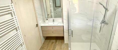 Een moderne badkamer met een douchecabine van glas, een witte wastafel en een houten vloer.