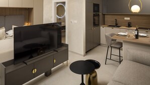 A modern living room with a flat-screen TV, a sofa, a coffee table, and a kitchen area with a dining table and bar stools. - Villa Maja Aurelia in the Centre- Romantic Studio Apartment (Hvar)
