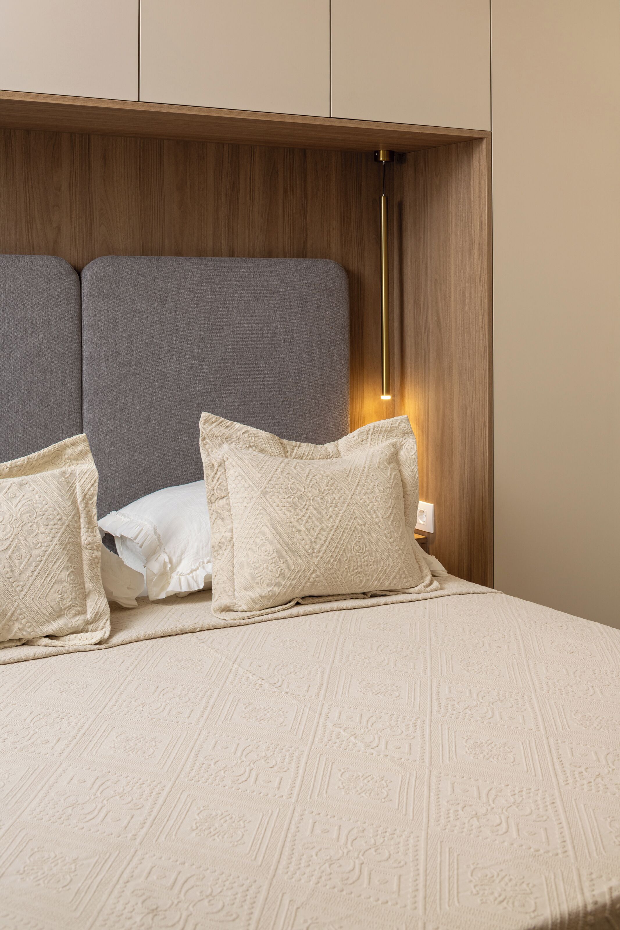 A neatly made bed with a textured white bedspread, a grey headboard, and two decorative pillows.