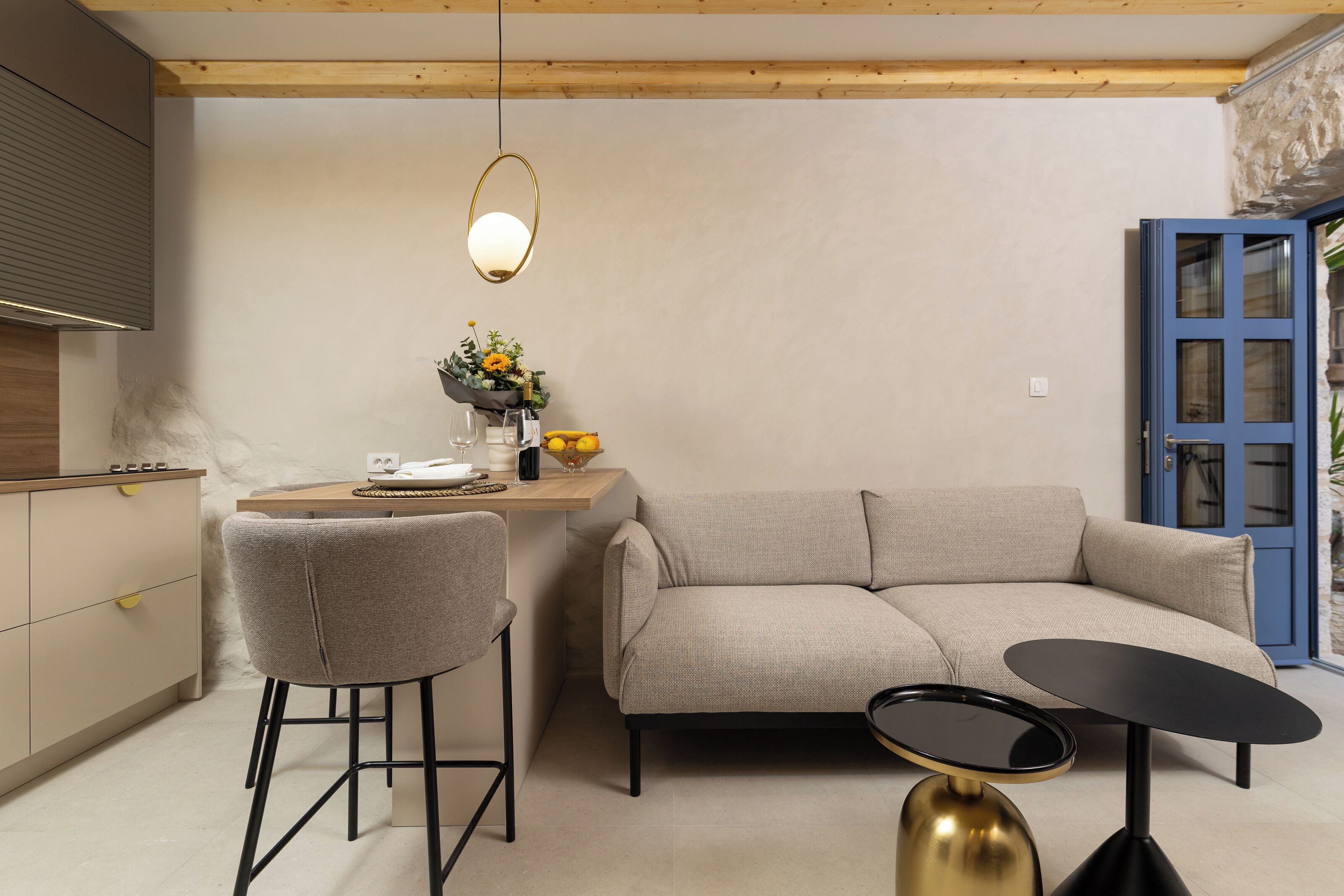 A modern living room with a sofa, a small round table, a bar stool, and a hanging light fixture.