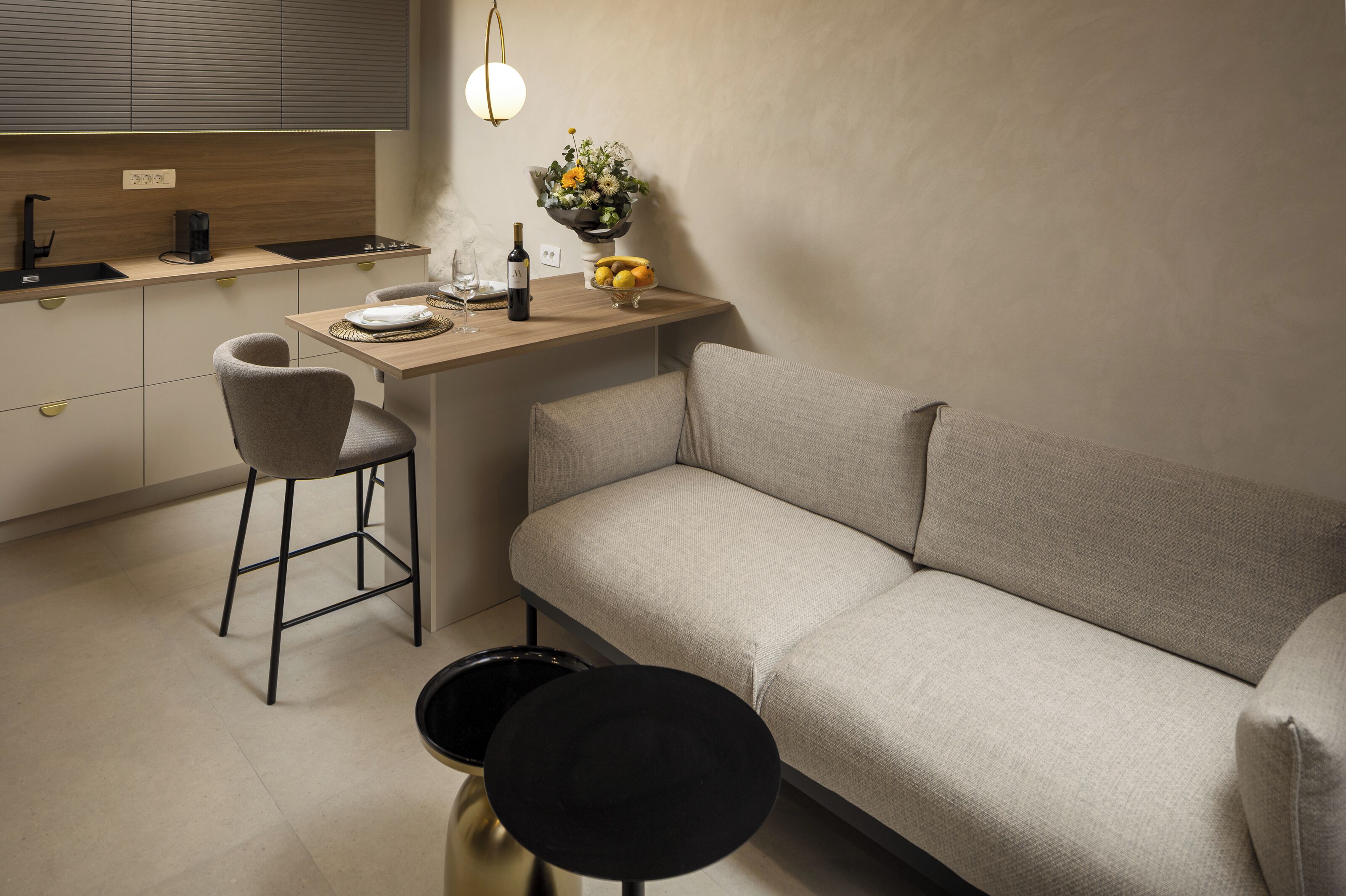 Un espacio habitable compacto con kitchenette, un sofá, una pequeña mesa de comedor y un taburete de bar.