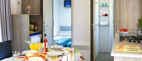 A compact hotel room with a dining area, kitchenette, and a bed.