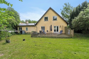 Ein zweistöckiges Haus mit umzäuntem Garten, einer Terrasse mit Gartenmöbeln und einem kleinen Gartenbereich.