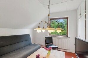 A modern living room with a sofa, a chair, a table with flowers, and a window with a view of greenery.
