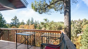 Une terrasse en bois avec une table en verre et deux chaises, donnant sur une zone boisée aux couleurs automnales.