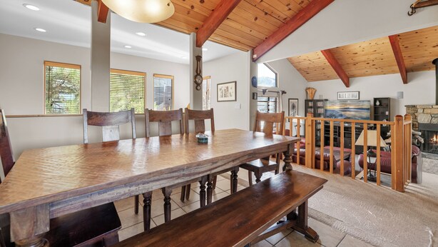 Un vaste espace dédié à la salle à manger, avec une grande table et des bancs en bois, des poutres apparentes au plafond et une vue sur une cheminée en pierre.