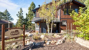 Une cabane avec une pancarte indiquant son nom et son numéro, entourée d’un jardin aménagé avec des rochers et des arbres.