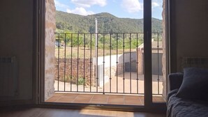 Una habitación con puerta corrediza de vidrio que da a un espacio exterior con vista a una montaña y un muro de piedra.