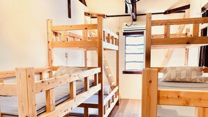 A room with two bunk beds made of wood, a window with blinds, and a ceiling fan. - Shimanto Hutte - Hostel (Shimanto)