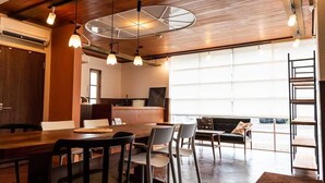 A modern interior with a wooden ceiling, a dining area with a table and chairs, a sofa, and a view of the outside. - Shimanto Hutte - Hostel (Shimanto)