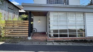 A white house with a garage door, a wooden fence, and a bicycle parked outside. - Shimanto Hutte - Hostel (Shimanto)
