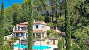 A two-story house with a swimming pool, surrounded by trees and greenery.