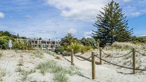 A beachfront property with a sandy pathway leading to a building, surrounded by greenery and a clear sky.
