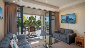 A modern living room with a sofa, a glass coffee table, and a TV mounted on the wall.