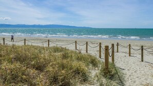 A sandy beach with a wooden fence and a person walking.